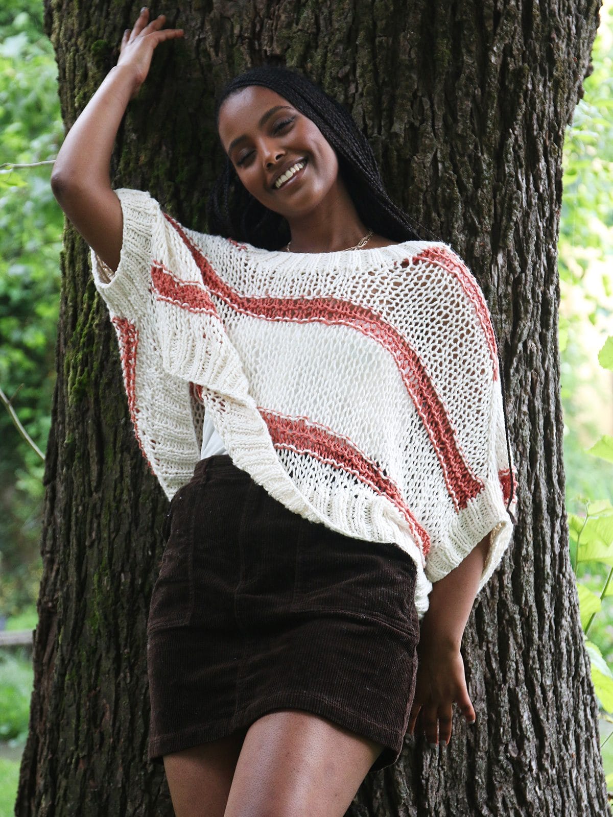 Dame i hvit strikket poncho topp med oransje striper. Strikkeoppskrift og strikkepakke - Sommerponcho er en luftig sommertopp strikket i økologisk bomull. Strikkes ovenfra og ned på tykke pinner.